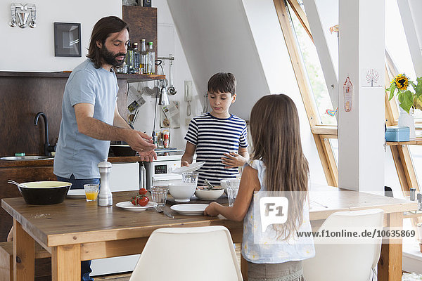 Father and children setting table for lunch in kitchen