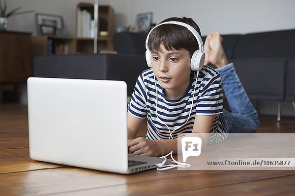 Junge  der Musik über Kopfhörer hört  während er den Laptop zu Hause benutzt.