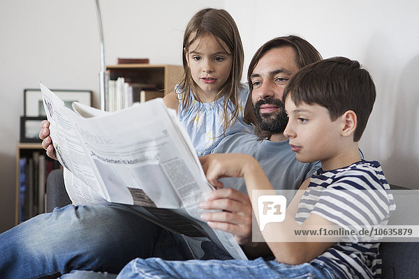 Vater und Kinder lesen Zeitung auf dem Sofa zu Hause