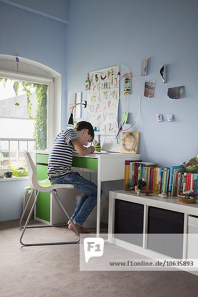 Side view of boy doing homework at table in house