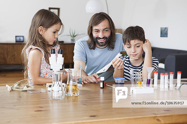 Glücklicher Vater und Kinder  die zu Hause ein naturwissenschaftliches Schulprojekt machen.