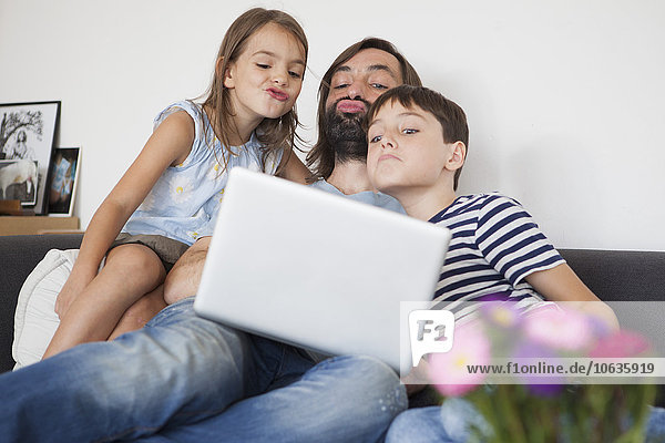 Vater mit Kindern  die auf dem Sofa vor dem Laptop kräuseln