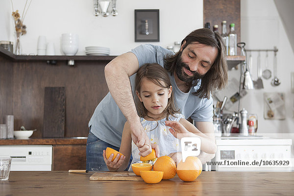 Father assisting daughter squeeze oranges in kitchen
