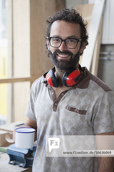 Porträt eines glücklichen mittelgroßen Schreiners beim Kaffee in der Werkstatt
