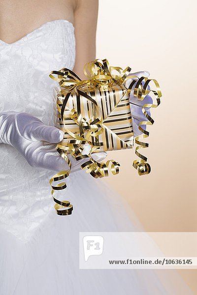 Midsection of bride holding gift box against colored background