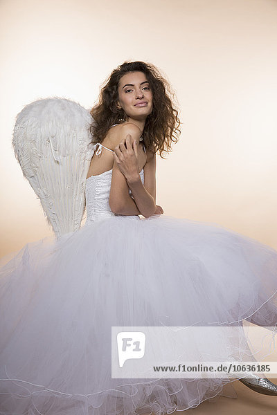 Portrait of smiling bride wearing angel wings against colored background