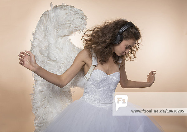 Bride in angel wings dancing while listening music against colored background