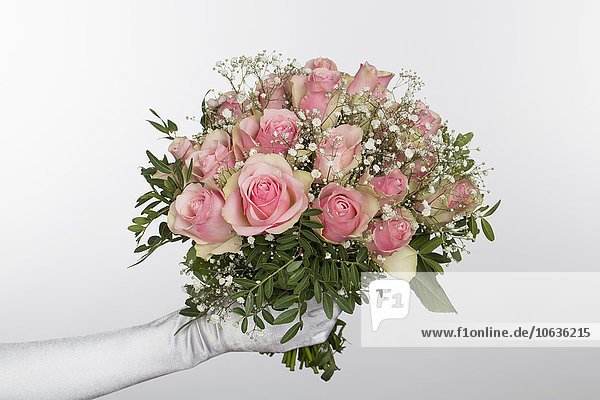 Cropped hand of bride holding bouquet against white background