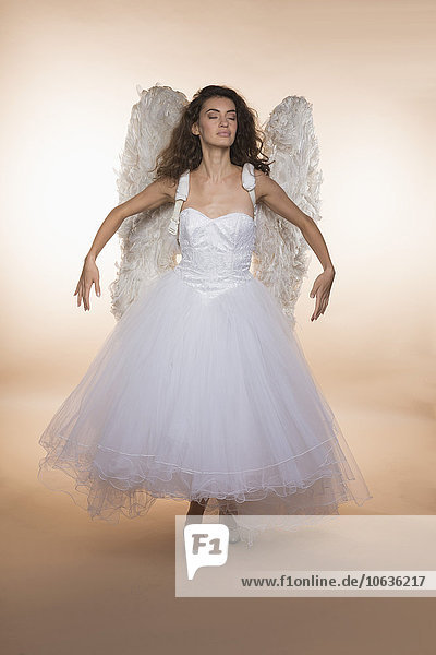 Bride with eyes closed wearing angel wings while standing against colored background
