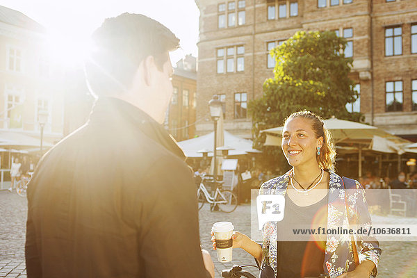 Smiling woman talking with male friend in city during summer