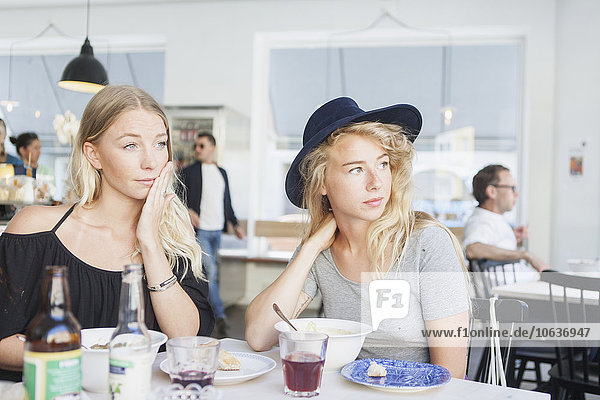 Thoughtful women looking away while sitting at restaurant table