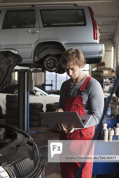 Mittlerer Erwachsener Mechaniker mit Laptop in der Garage