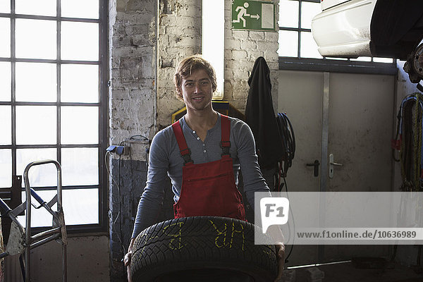 Porträt eines lächelnden Mechanikers  der den Reifen in der Garage hält.