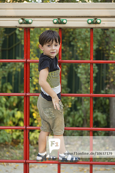 Porträt eines Jungen  der auf einer Kletterwand im Park steht