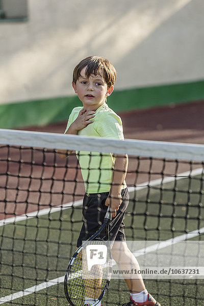 Boy holding tennis racket while standing on field