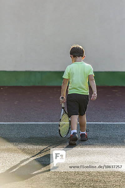 Rückansicht des Jungen mit Tennisschläger und Spaziergang auf dem Platz