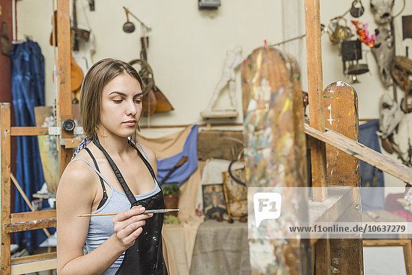 Malerin mit Pinsel und Blick auf Staffelei im Atelier