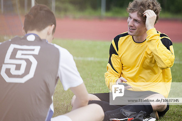 Young sportsman sitting with friend on soccer field