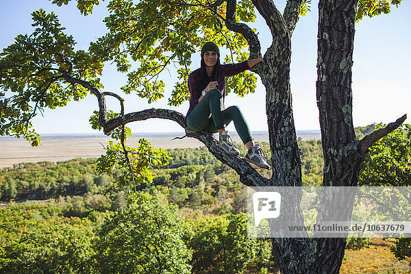 Ganzflächiges Porträt einer jungen Frau auf einem Baum im Wald