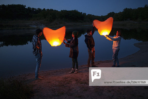 Full length of hikers releasing paper lanterns at lakeshore