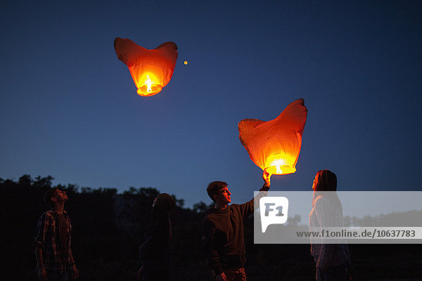 Low angle view of friends with paper lanterns in forest