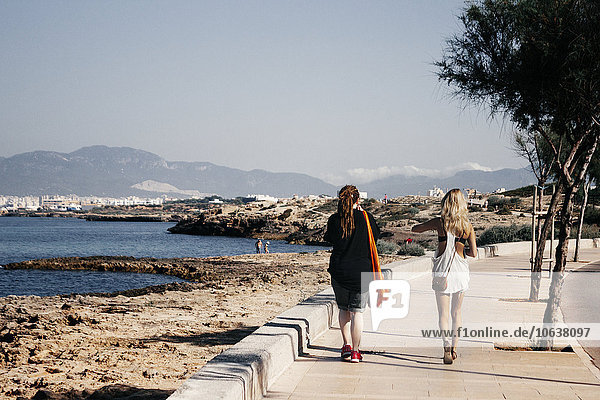 Full length rear view of women walking on footpath by sea