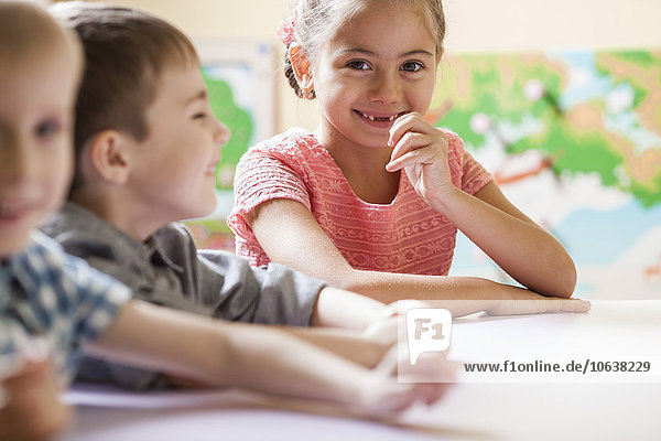 Porträt eines glücklichen kleinen Mädchens mit Freunden am Tisch im Klassenzimmer