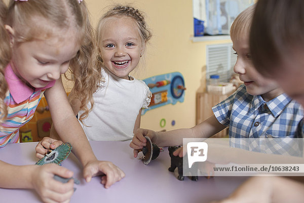 Portrait of cheerful girl with friends playing with toy animals at table in classroom