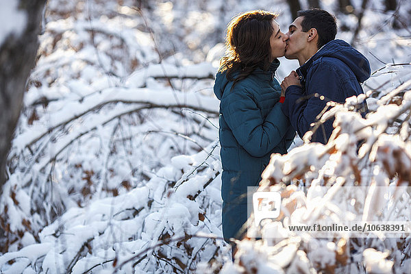 Side view of young couple kissing by snow covered trees