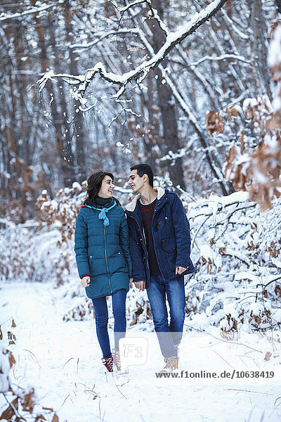 Full length of loving young couple in warm clothing walking on snowy field