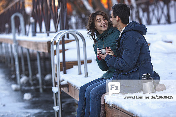Happy young couple having coffee while sitting on pier