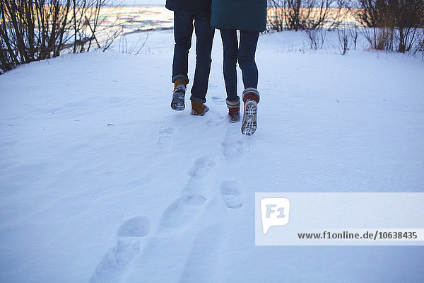 Low section of young couple walking on snowy field