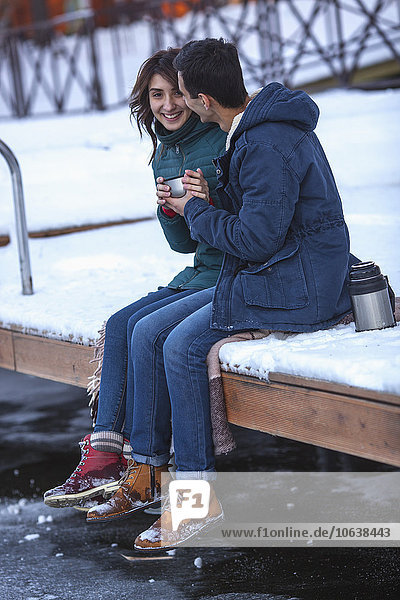 Full length of happy young couple having coffee on pier
