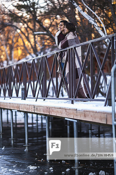 Young couple wrapped in blanket on bridge during winter