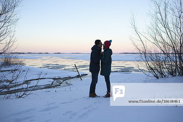 Full length side view of young couple kissing on snowy field