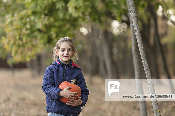 Porträt eines lächelnden Mädchens mit Kürbis im Wald