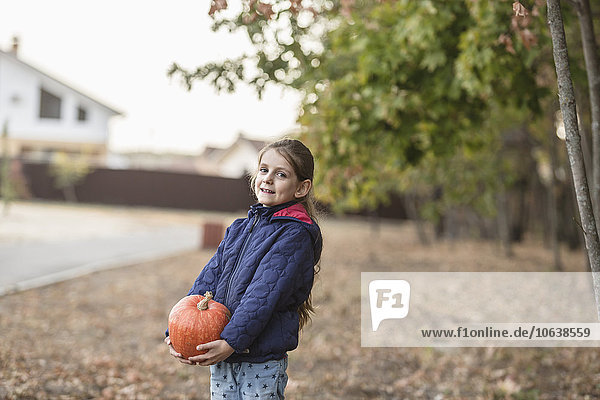 Portrait of cute girl holding pumpkin outdoors