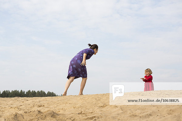 Mutter und Tochter spielen auf Sand gegen den Himmel