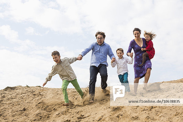 Family holding hands while enjoying on sand dune against sky