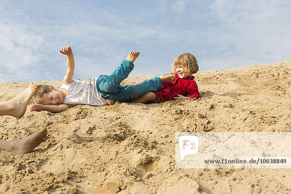 Geschwister genießen auf Sanddüne gegen den Himmel