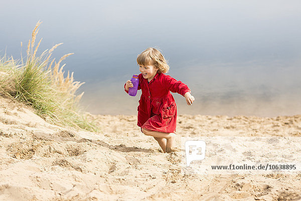 Fröhliches Mädchen mit Wasserflasche beim Laufen auf der Sanddüne