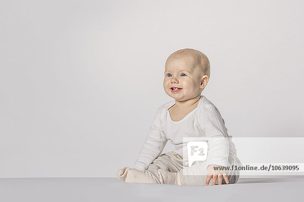 Fröhliches kleines Mädchen sitzend vor weißem Hintergrund