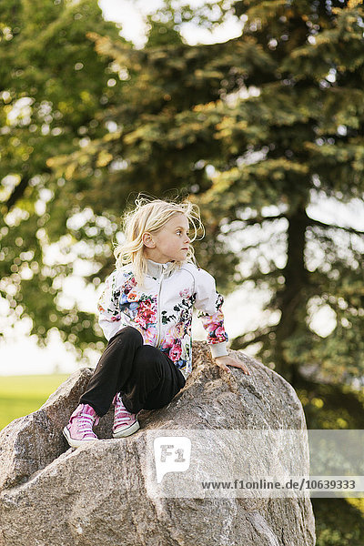 Girl looking away while sitting on rock at field