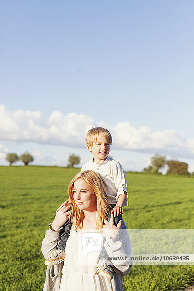 Pregnant woman carrying son on shoulders at field