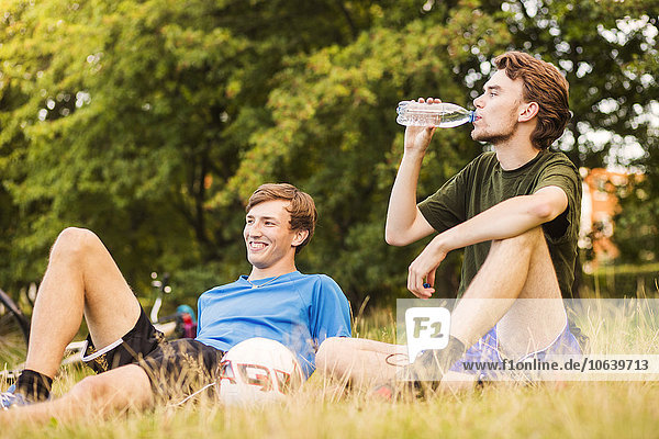 Young sporty man drinking water while relaxing with friend at park