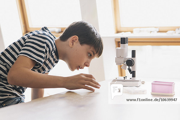 Neugieriger Junge schaut sich das Mikroskop auf dem Tisch im Haus an.