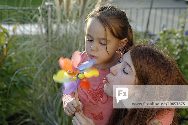 Two girls blowing colourful toy pinwheel  Germany  Europe