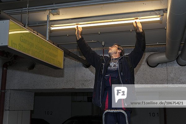 Hausmeister wechselt Leuchtstofflampe in einer Tiefgarage