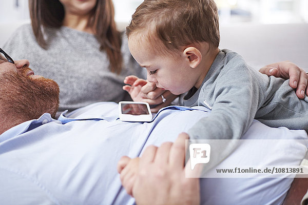 Neugieriges Kleinkind beim Blick auf das Handy auf Vaters Brust