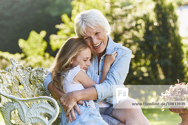 Großmutter und Enkelin umarmend auf der Gartenbank